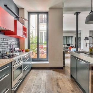 Réalisation d'une grand cuisine ouverte parallèle design avec un évier encastré, un plan de travail en inox, un sol en bois brun, un plan de travail gris, un placard à porte plane, des portes de placard grises, une crédence grise, une crédence en brique, un électroménager en acier inoxydable, un îlot central et un sol marron.
