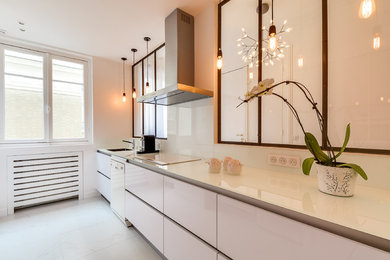 パリにある高級な広いコンテンポラリースタイルのおしゃれなキッチン (シングルシンク、白いキャビネット、白いキッチンパネル、白い調理設備、アイランドなし、フラットパネル扉のキャビネット、ガラス板のキッチンパネル) の写真