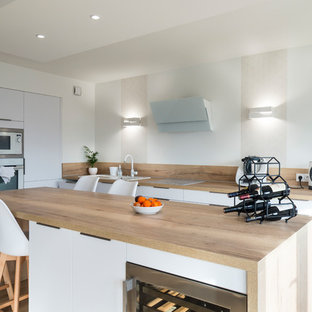 Cette photo montre une grand cuisine scandinave avec des portes de placard blanches, un plan de travail en bois, une crédence beige, une crédence en bois, un sol en bois clair, un îlot central, un sol beige, un plan de travail beige, un évier posé, un placard à porte plane et un électroménager blanc.