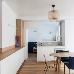Cette photo montre une cuisine américaine tendance avec un évier encastré, un placard à porte plane, des portes de placard blanches, un électroménager encastrable, un sol en bois brun, 2 îlots, un sol marron et un plan de travail gris.