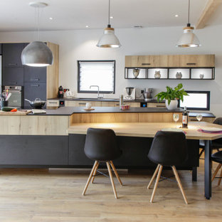 Cette image montre une cuisine parallèle design avec un évier encastré, un placard à porte plane, des portes de placard en bois clair, un électroménager en acier inoxydable, un sol en bois clair, un îlot central, un sol beige et un plan de travail gris.
