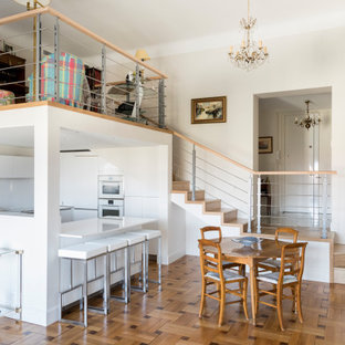 Cette photo montre une cuisine ouverte tendance en U avec un placard à porte plane, des portes de placard blanches, un électroménager blanc, un sol en bois brun, une péninsule, un sol marron et un plan de travail blanc.