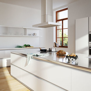 Inspiration pour une cuisine parallèle minimaliste avec un évier encastré, un placard à porte plane, des portes de placard blanches, un électroménager noir, un sol en bois clair, 2 îlots et un sol orange.