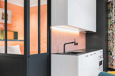 Design ideas for a contemporary single-wall open plan kitchen in Nantes with a built-in sink, flat-panel cabinets, white cabinets, pink splashback, glass sheet splashback, white appliances, light hardwood flooring, beige floors and black worktops.