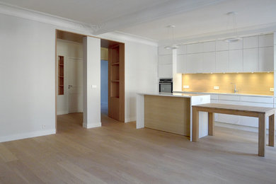 Cette photo montre une grande cuisine ouverte parallèle tendance avec parquet clair, des portes de placard blanches et îlot.