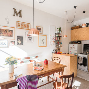 Aménagement d'une cuisine américaine éclectique avec un placard à porte plane, des portes de placard en bois clair, un plan de travail en bois, un électroménager blanc, une péninsule et un sol beige.