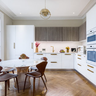 Idées déco pour une cuisine américaine contemporaine en L avec un placard à porte plane, des portes de placard blanches, une crédence blanche, un électroménager encastrable, un sol en bois brun et un plan de travail blanc.