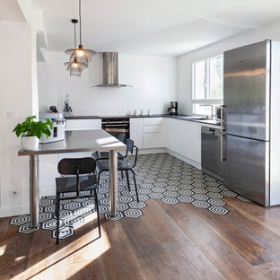 Cette image montre une cuisine ouverte design en U avec un évier intégré, des portes de placard blanches, un plan de travail en quartz modifié, une crédence blanche, un sol noir, un placard à porte plane, un électroménager en acier inoxydable, une péninsule et un plan de travail noir.
