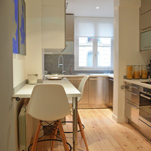 Aménagement d'une cuisine parallèle contemporaine fermée et de taille moyenne avec un évier encastré, un placard à porte plane, une façade en inox, une crédence grise, un électroménager en acier inoxydable, un sol en bois clair et aucun îlot.