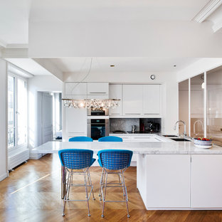Aménagement d'une grand cuisine ouverte contemporaine en U avec un évier encastré, un placard à porte plane, des portes de placard blanches, un plan de travail en marbre, un électroménager en acier inoxydable, un sol en bois clair et une péninsule.