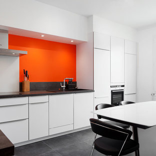 Cette image montre une grand cuisine américaine design en L avec des portes de placard blanches, un sol en carrelage de céramique, aucun îlot et une crédence orange.