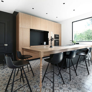 Réalisation d'une cuisine parallèle design avec un placard à porte plane, des portes de placard en bois brun, un plan de travail en bois, une crédence noire, un électroménager en acier inoxydable, un îlot central, un sol gris et un plan de travail marron.