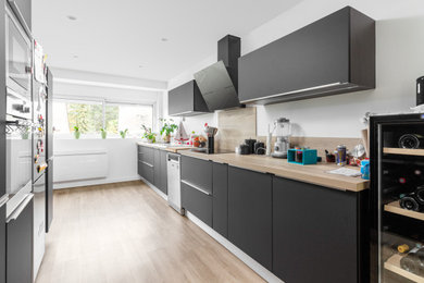 Cette image montre une grande cuisine ouverte parallèle et encastrable minimaliste avec des portes de placard noires, un plan de travail en bois, une crédence en bois et sol en stratifié.