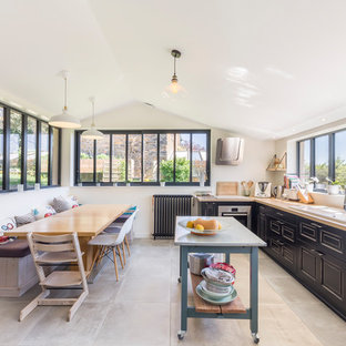 Cette photo montre une cuisine américaine chic en L avec un évier posé, un placard avec porte à panneau surélevé, des portes de placard noires, un plan de travail en bois, un électroménager en acier inoxydable, un sol en carreaux de ciment, un îlot central et un sol gris.
