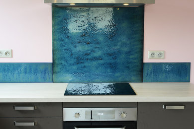 Inspiration pour une cuisine ouverte design en L de taille moyenne avec une crédence bleue, une crédence en feuille de verre et aucun îlot.