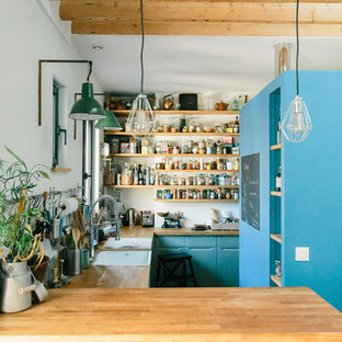 Cette photo montre une cuisine industrielle en U avec un évier encastré, un placard à porte plane, des portes de placard turquoises, un plan de travail en bois, une crédence blanche, une péninsule et un plan de travail marron.