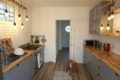 パリにある高級な中くらいなモダンスタイルのおしゃれな独立型キッチン (アンダーカウンターシンク、落し込みパネル扉のキャビネット、グレーのキャビネット、木材カウンター、白いキッチンパネル、レンガのキッチンパネル、シルバーの調理設備、セメントタイルの床、グレーの床、茶色いキッチンカウンター) の写真