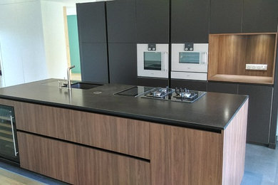 Cette photo montre une cuisine ouverte parallèle moderne de taille moyenne avec des portes de placard marrons, îlot, un sol gris et plan de travail noir.