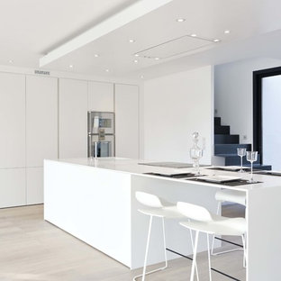 Inspiration pour une grand cuisine américaine linéaire design avec des portes de placard blanches, un électroménager en acier inoxydable, un sol en bois clair et un îlot central.
