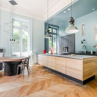 This is an example of a large modern single-wall eat-in kitchen in Lyon with an undermount sink, beaded inset cabinets, light wood cabinets, black splashback, marble splashback, black appliances, light hardwood floors, with island, beige floor and black benchtop.
