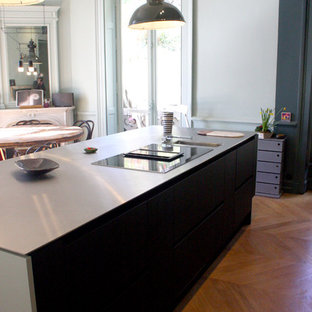 Large modern single-wall eat-in kitchen in Lyon with an undermount sink, black splashback, marble splashback, light hardwood floors, beige floor, beaded inset cabinets, light wood cabinets, black appliances, with island and black benchtop.