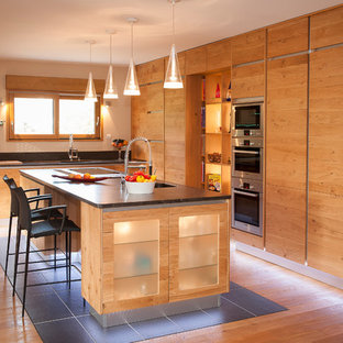 Cette image montre une grand cuisine américaine chalet en L avec un placard à porte plane, des portes de placard en bois brun, un électroménager en acier inoxydable, un sol en bois brun et un îlot central.