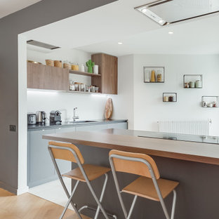 Inspiration pour une cuisine design en L avec un évier encastré, un placard à porte plane, des portes de placard grises, une péninsule, un sol blanc et un plan de travail noir.