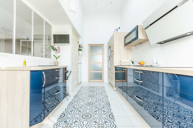 他の地域にある広いコンテンポラリースタイルのおしゃれなキッチン (青いキャビネット、ラミネートカウンター、パネルと同色の調理設備、セメントタイルの床、白い床、シングルシンク、白いキッチンパネル、ガラス板のキッチンパネル、アイランドなし) の写真