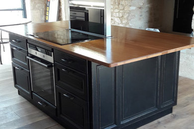This is an example of a large traditional single-wall open plan kitchen in Other with a submerged sink, black cabinets, wood worktops, brown splashback, wood splashback, stainless steel appliances, light hardwood flooring, an island, beige floors and brown worktops.
