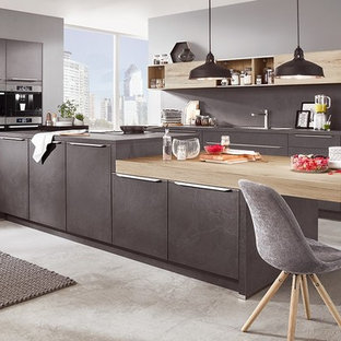 Aménagement d'une très grand cuisine ouverte contemporaine en U avec des portes de placard grises, une crédence grise, un électroménager en acier inoxydable, béton au sol, un îlot central et un sol gris.