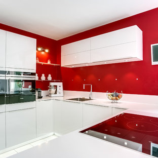 Inspiration pour une cuisine américaine design en U avec un évier encastré, un placard à porte plane, des portes de placard blanches, une crédence rouge et un électroménager blanc.