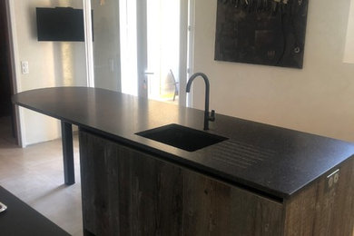 Inspiration for a medium sized modern galley open plan kitchen in Marseille with a submerged sink, flat-panel cabinets, dark wood cabinets, granite worktops, black appliances, ceramic flooring, an island, grey floors and black worktops.