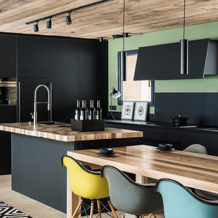 Idées déco pour une cuisine américaine parallèle contemporaine de taille moyenne avec un évier posé, un placard à porte plane, des portes de placard beiges, un plan de travail en bois, une crédence noire, un électroménager noir, un sol en bois clair, un îlot central, un sol beige et un plan de travail marron.