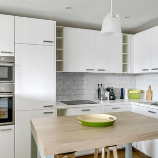 Idée de décoration pour une cuisine ouverte design en L de taille moyenne avec une crédence blanche, une crédence en carrelage métro, un sol en bois clair, un évier 1 bac, un placard à porte plane, des portes de placard blanches, un plan de travail en stratifié, un électroménager en acier inoxydable et un îlot central.