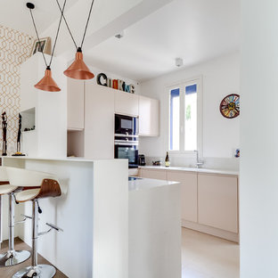 Aménagement d'une petit cuisine américaine contemporaine en U avec un placard à porte plane, des portes de placard beiges, un électroménager noir, une péninsule, un évier encastré et une crédence grise.