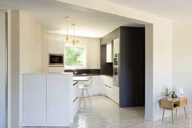 Design ideas for a medium sized contemporary l-shaped open plan kitchen in Rennes with flat-panel cabinets, white cabinets, beige splashback, stainless steel appliances, ceramic flooring, no island and beige floors.
