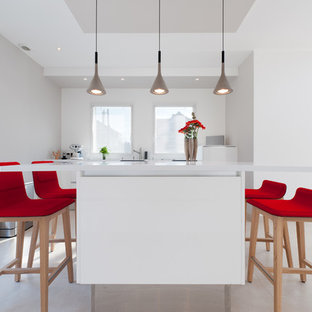 Réalisation d'une grand cuisine américaine linéaire design avec un évier intégré, un placard à porte affleurante, des portes de placard blanches, un plan de travail en quartz, un électroménager encastrable et un îlot central.