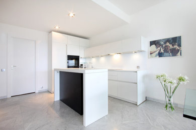 Cette image montre une cuisine ouverte parallèle et encastrable minimaliste de taille moyenne avec des portes de placard blanches, un sol en marbre et îlot.