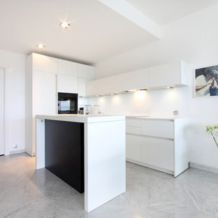 Cette image montre une cuisine ouverte parallèle minimaliste de taille moyenne avec des portes de placard blanches, un électroménager encastrable, un sol en marbre et un îlot central.