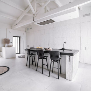 Exemple d'une grand cuisine ouverte linéaire bord de mer avec des portes de placard blanches, un plan de travail en granite, un sol en carrelage de céramique, un îlot central, un plan de travail noir, un évier 1 bac, un placard à porte plane et un sol blanc.