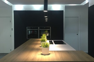 Cette image montre une grande cuisine ouverte parallèle minimaliste avec un placard à porte vitrée, des portes de placard noires, un plan de travail en bois, un électroménager noir, sol en béton ciré, îlot et un sol gris.