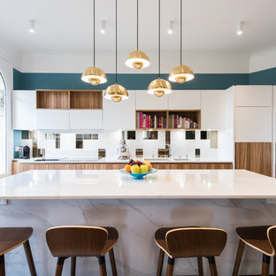Réalisation d'une cuisine design avec des portes de placard blanches, une crédence blanche, un électroménager en acier inoxydable, un îlot central, un évier 2 bacs et un placard à porte plane.