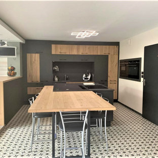 Photo of an expansive single-wall open plan kitchen in Lille with an integrated sink, beaded inset cabinets, grey cabinets, laminate benchtops, black splashback, stainless steel appliances, cement tiles, with island, white floor and brown benchtop.