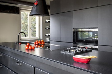Cette photo montre une cuisine ouverte industrielle avec une crédence noire, un électroménager noir, carreaux de ciment au sol, îlot et un sol gris.