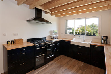 アンジェにある広いカントリー風のおしゃれなキッチン (ドロップインシンク、落し込みパネル扉のキャビネット、黒いキャビネット、木材カウンター、黒い調理設備) の写真