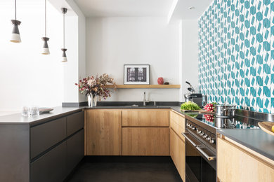 Aménagement d'une cuisine bicolore scandinave en U et bois clair avec un placard à porte plane, une crédence multicolore, une péninsule, un sol noir et un plan de travail gris.