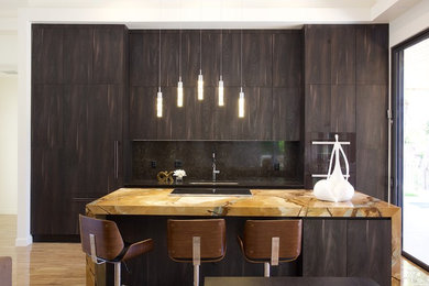 Foto di un grande cucina con isola centrale minimalista con lavello sottopiano, ante in legno bruno, top in quarzite e elettrodomestici neri