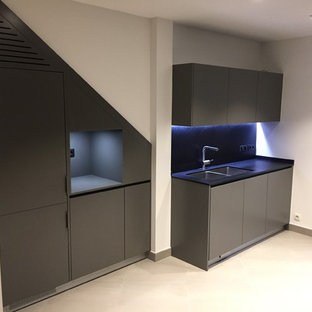 Imagen de cocina de galera, moderna, de tamaño medio, abierta, sin isla, con fregadero bajoencimera, armarios con paneles lisos, puertas de armario grises, encimera de granito, salpicadero negro, salpicadero de piedra caliza, electrodomésticos con paneles, suelo de baldosas de terracota, suelo beige y encimeras negras