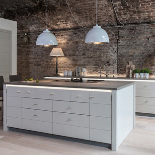 Idée de décoration pour une grand cuisine ouverte urbaine en L avec un évier encastré, un placard à porte plane, des portes de placard grises, une crédence marron, une crédence en brique, un électroménager noir, un sol en bois clair, un îlot central et un sol beige.