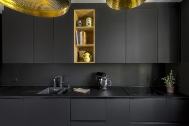 Cette image montre une grande cuisine parallèle design fermée avec un évier intégré, une crédence noire, un électroménager en acier inoxydable, îlot, un sol gris et plan de travail noir.